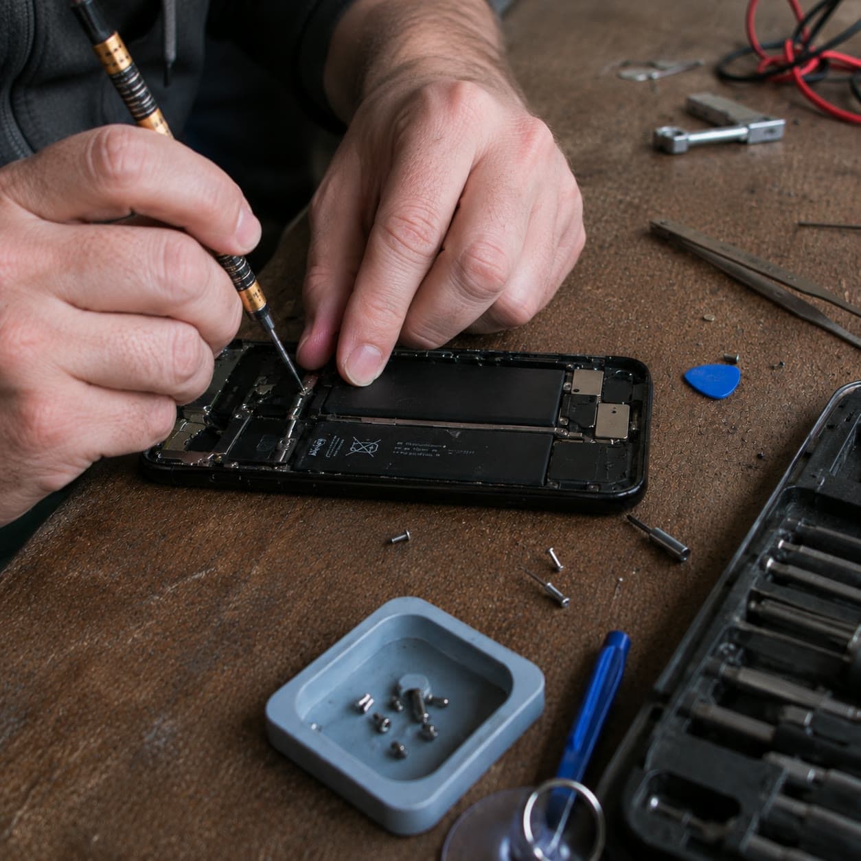 Manos reparando la placa de un celular con destornillador de precisión